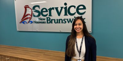 Une femme pose devant le logo de la Ligne d'écoute consacrée au traitement des dépendances et de la santé mentale au Nouveau-Brunswick